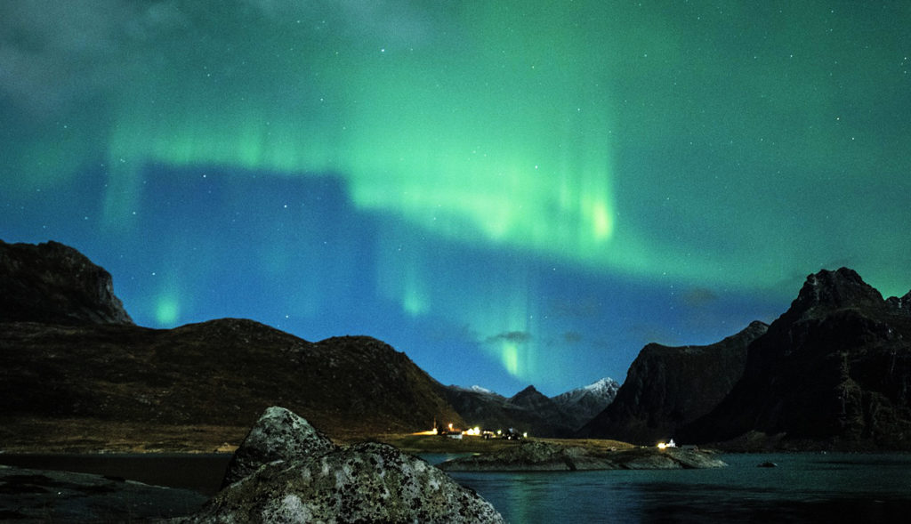 Un immagine suggestiva del fenomeno dei colori nell'aria luminescenti dell'aurora boreale sullo sfondo del fiordo dove sorgono le isole Lofoten che si vedono in lontananza